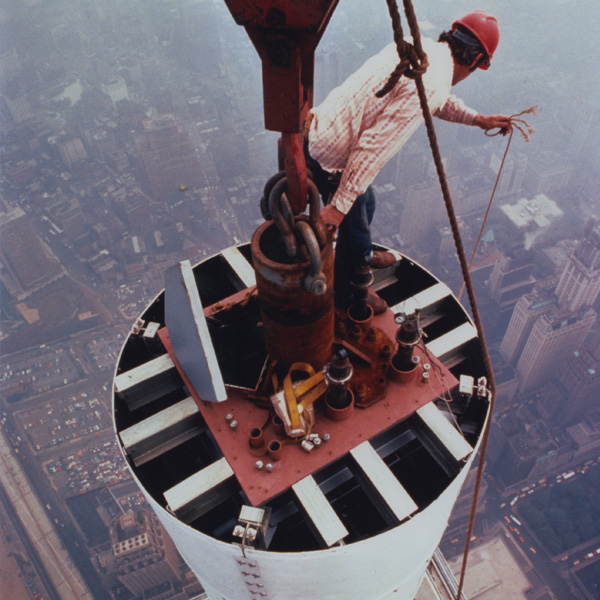 Photograph of a worker installing the antenna of the World Trade Center, looking down street level. Photograph by Peter B. Kaplan